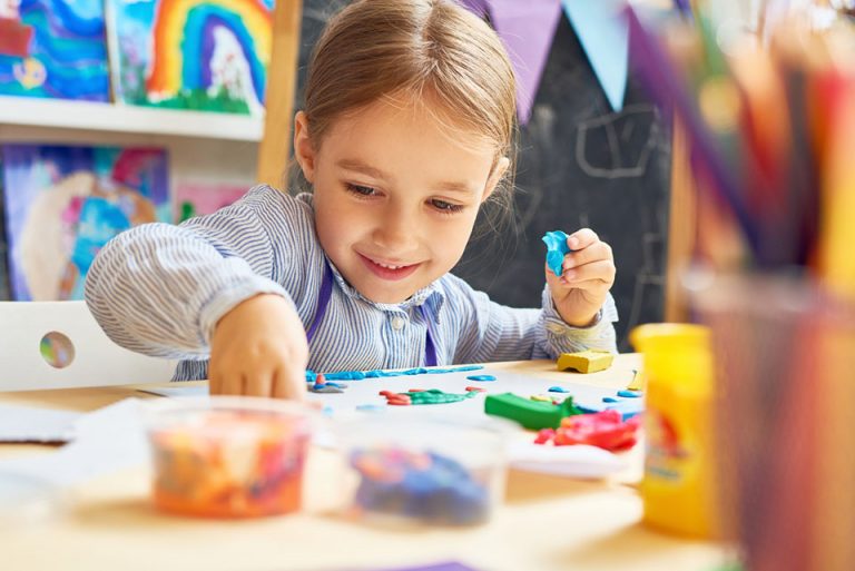 Portrait of smiling little girl working with plasticine in art and craft class of development school